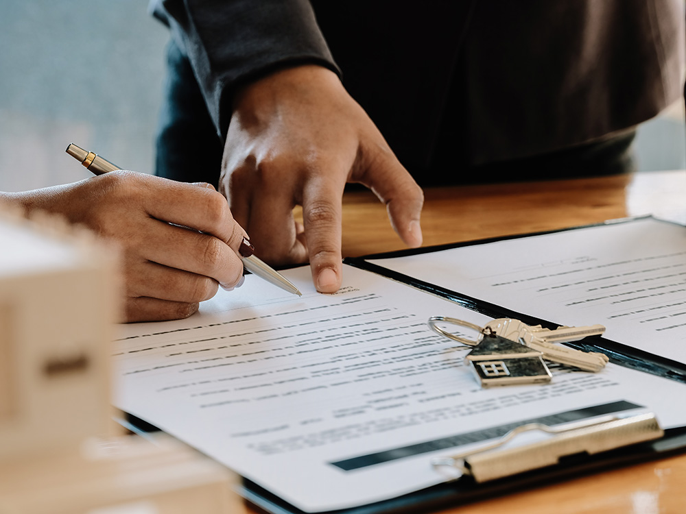 Two people reviewing and signing documents with a set of house keys on the table