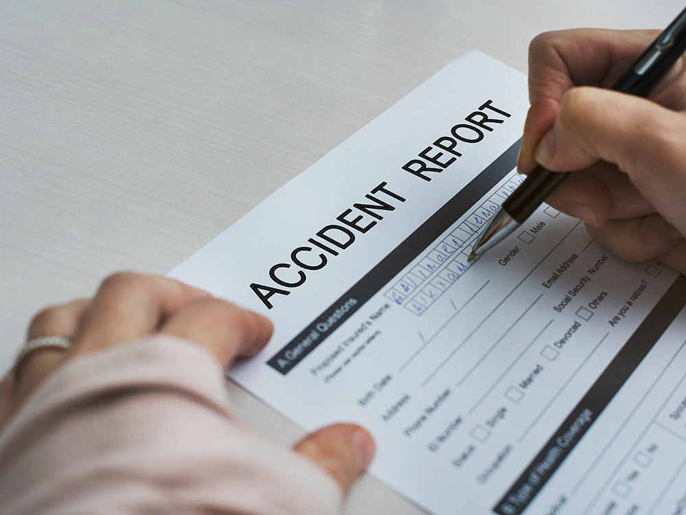 Person filling out an accident report form with a pen
