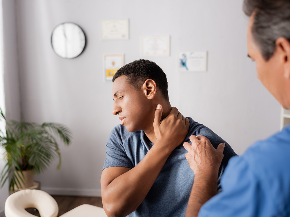 Man holding his neck in pain while a medical professional examines his shoulder