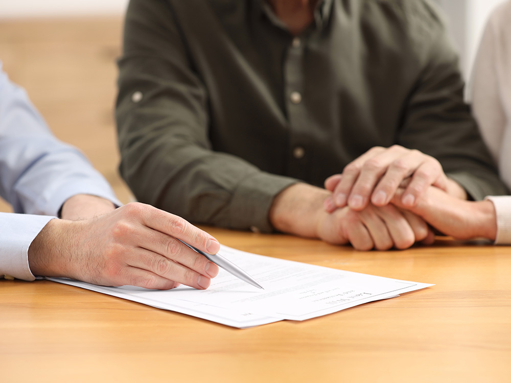 Person pointing to a document while two others hold hands across a table