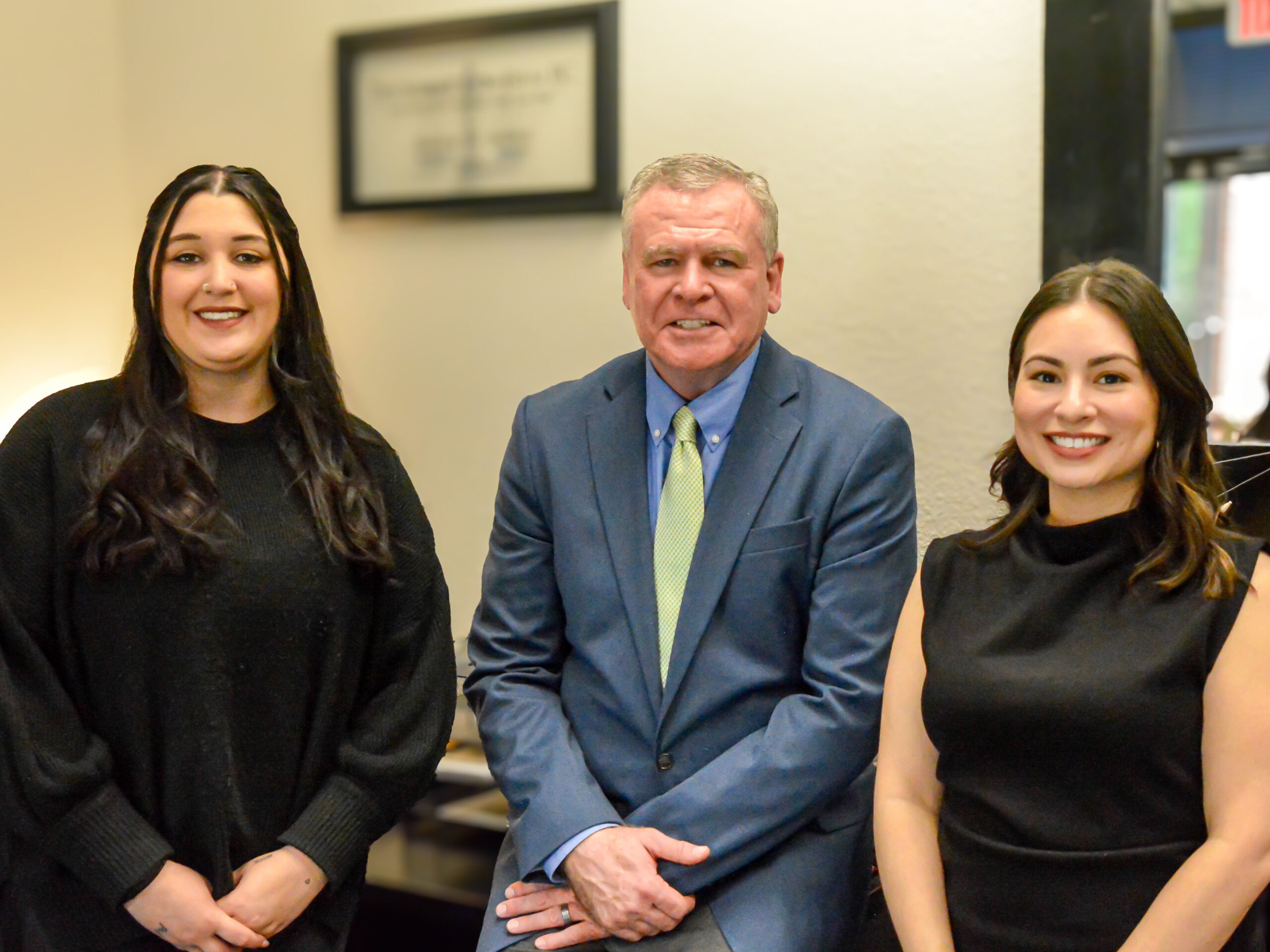 A man and two women smile at the camera from a well appointed conference room